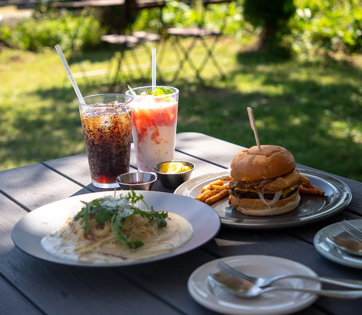 Burger, pasta, and drinks set on an outdoor table