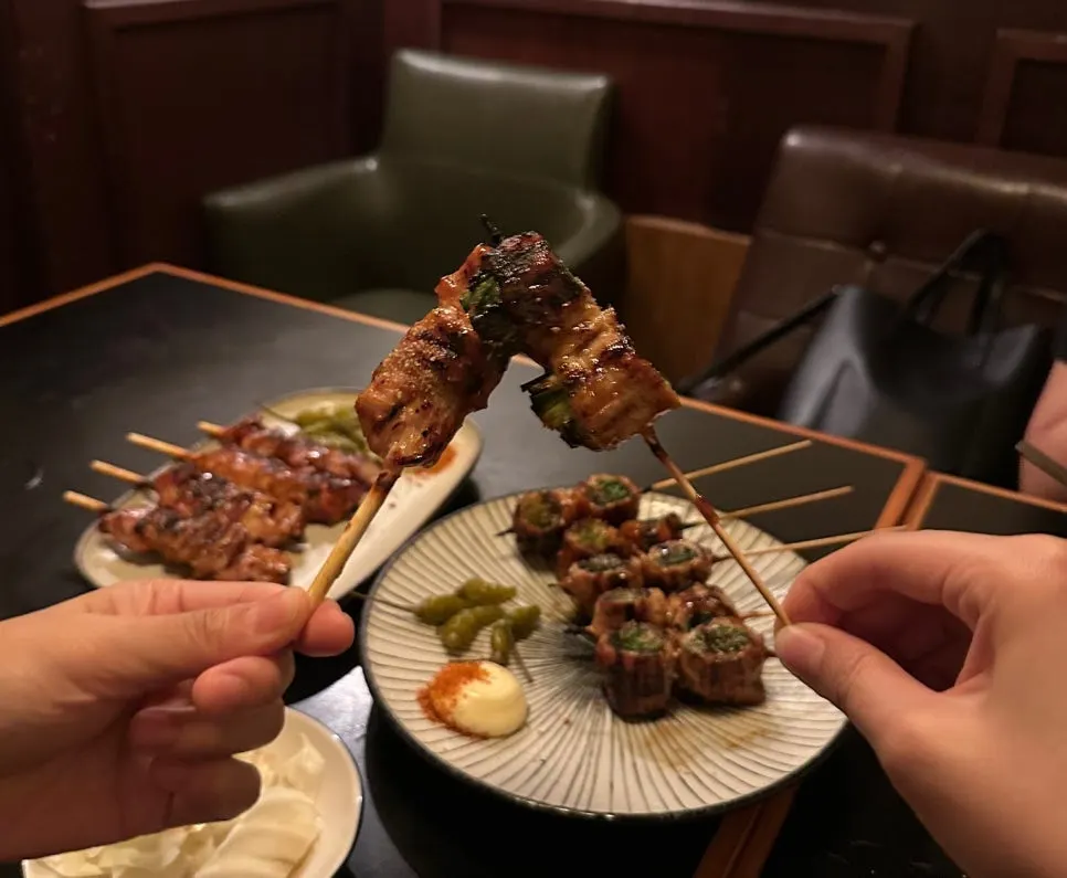 Two plates: chicken skewers and pork belly scallion skewers