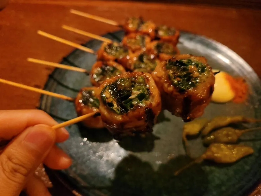 A plate of scallion pork belly skewers coated in teriyaki-style sauce