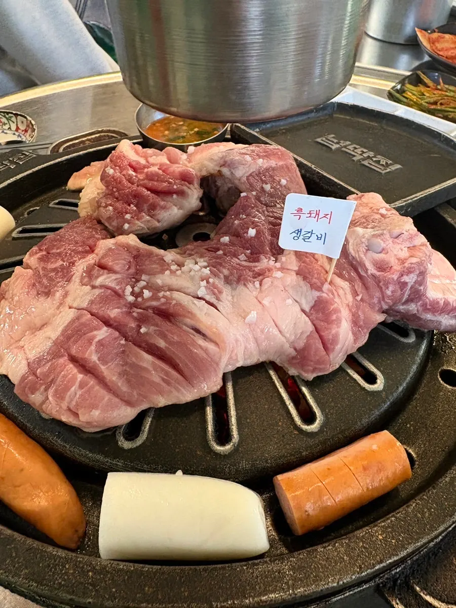 Raw ribs, rice cakes, and sausage grilling on the cast-iron pan
