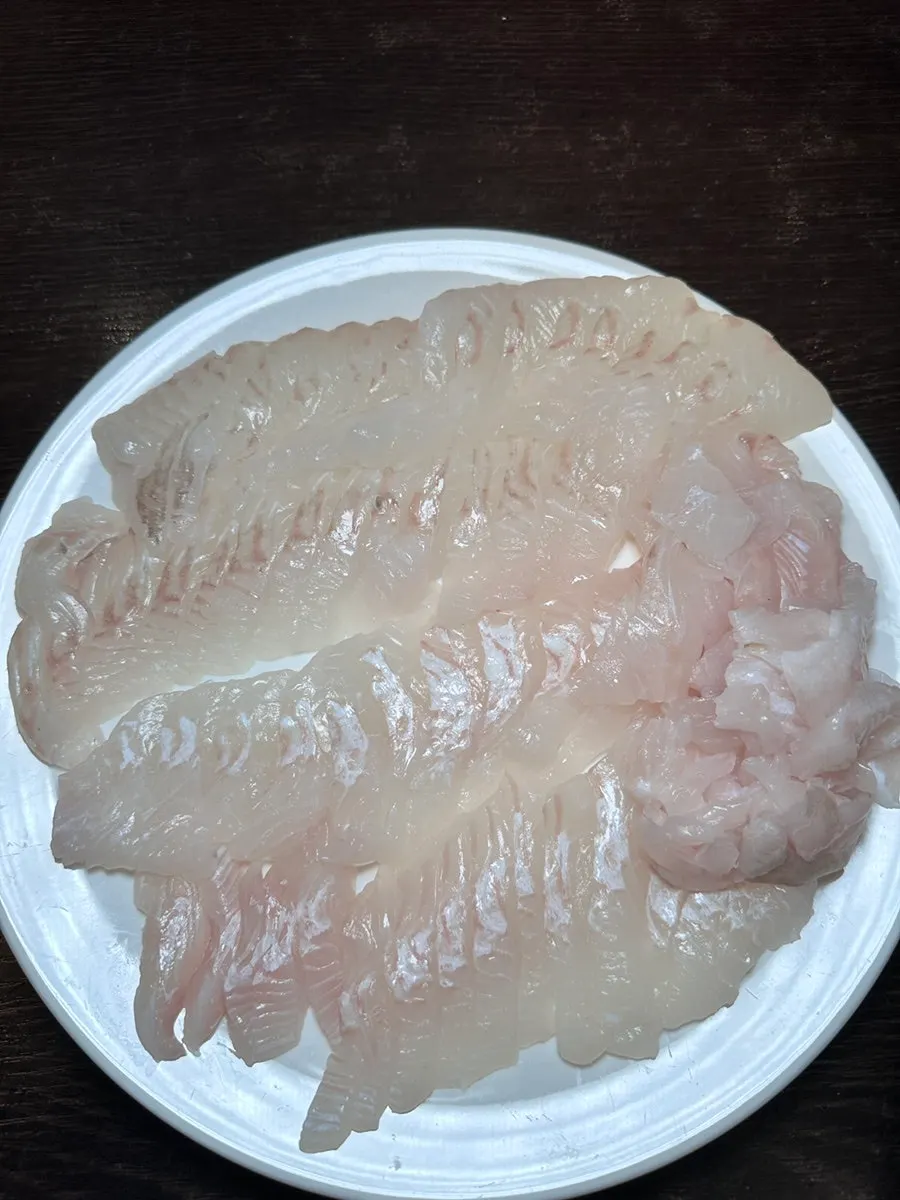 A piece of flounder sashimi picked up with chopsticks