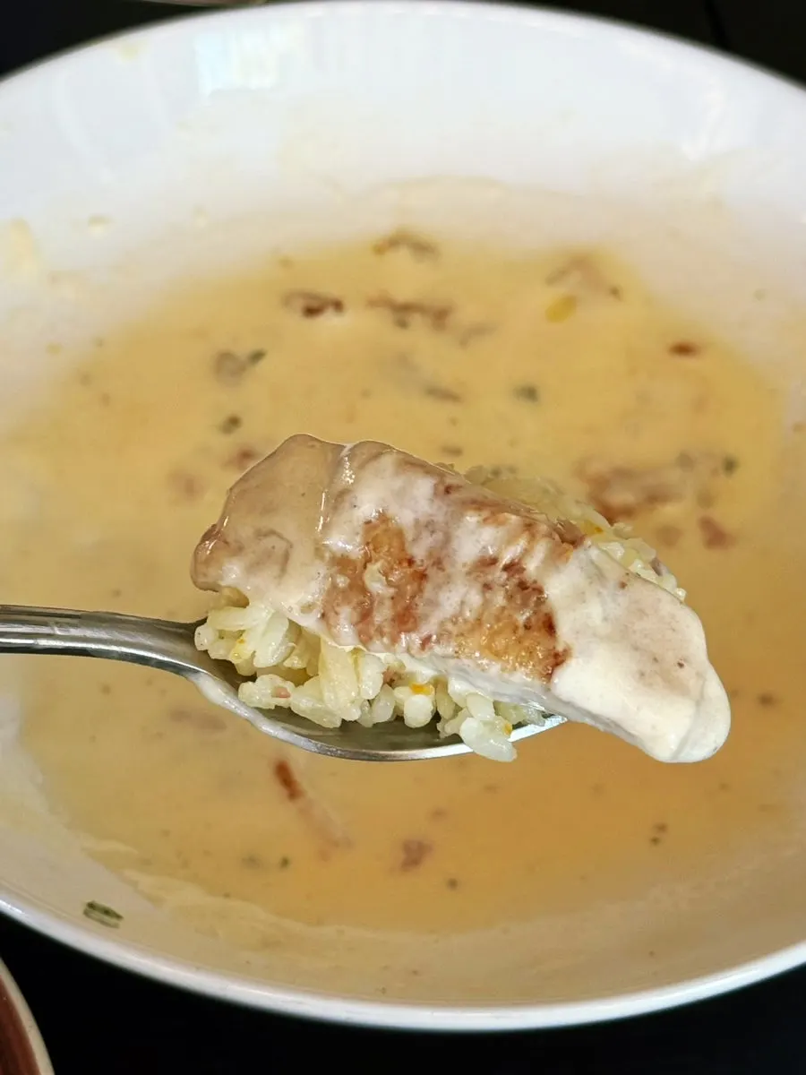A spoonful of butter rice topped with cream sauce and chicken thigh