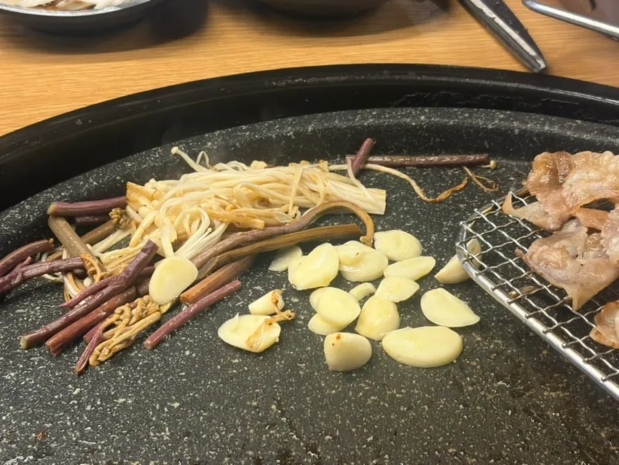 Garlic, enoki mushrooms, and bracken fern grilled together on the pan