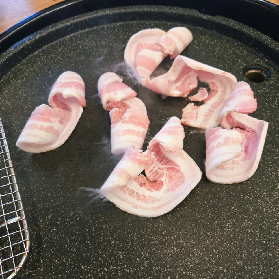 Thin-sliced pork belly grilling on the wide pan