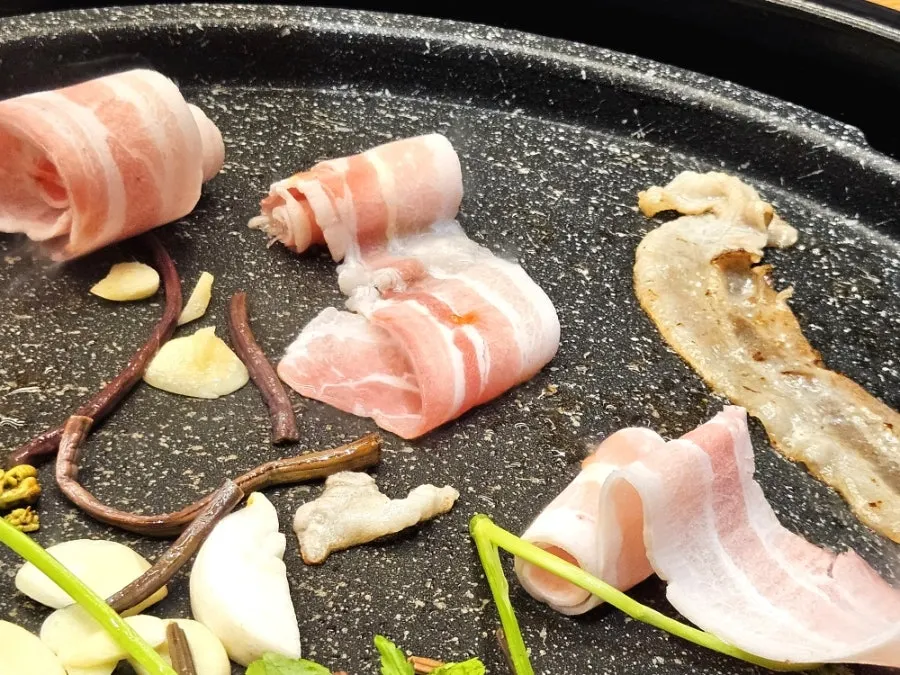 Thin-sliced pork belly cooking on the grill