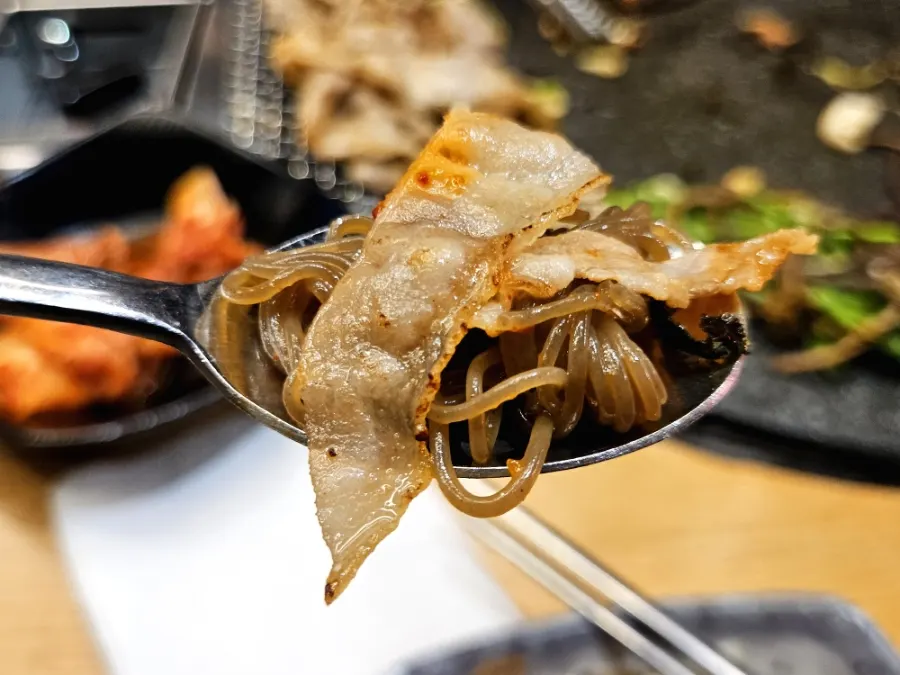A bite of bibim naengmyeon topped with pork belly