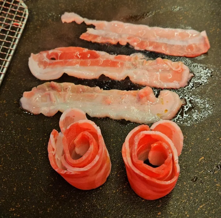 Sliced pork belly and accompaniments on a large grill