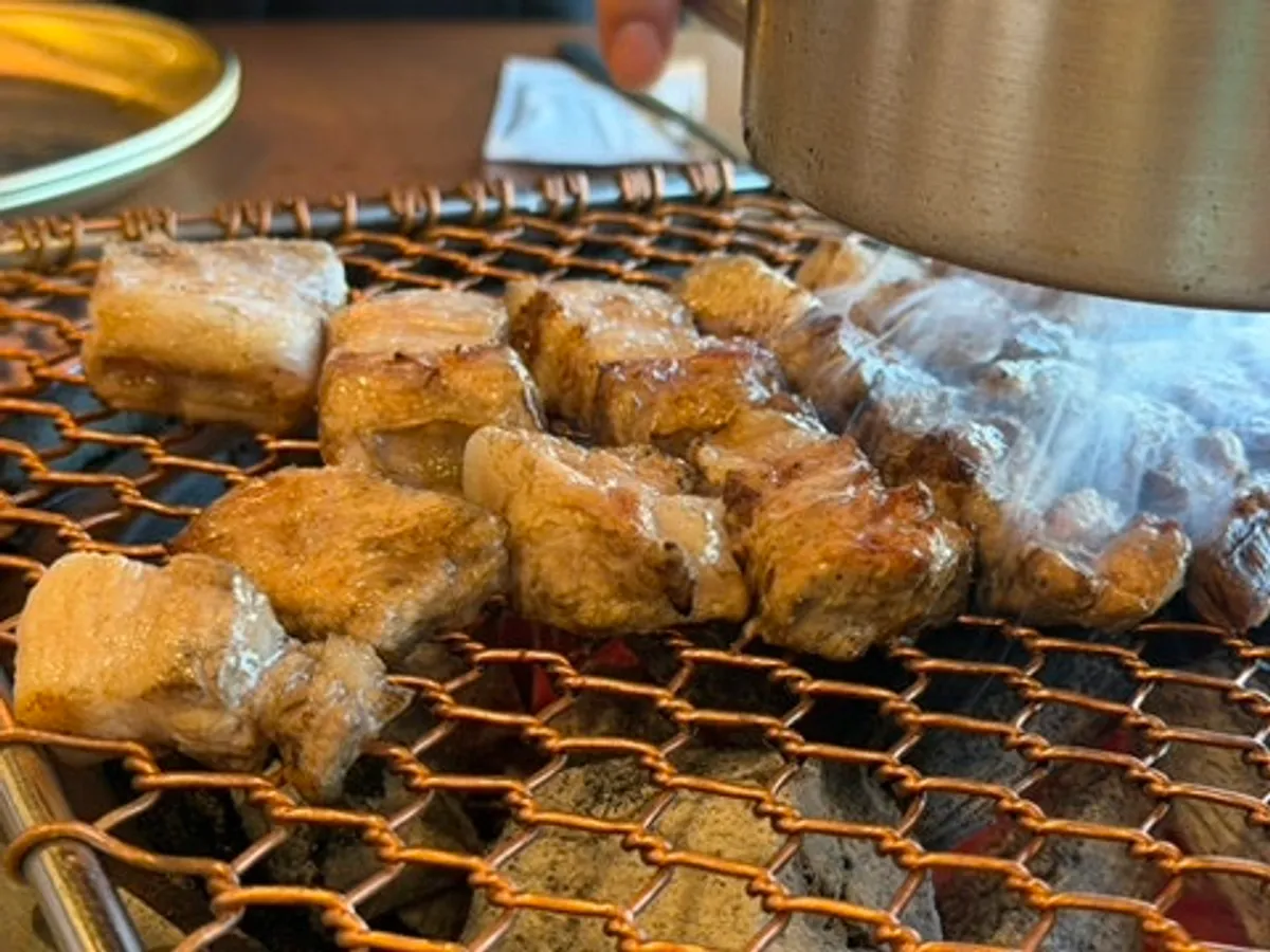 Table setup with bibim naengmyeon next to black pork on the grill