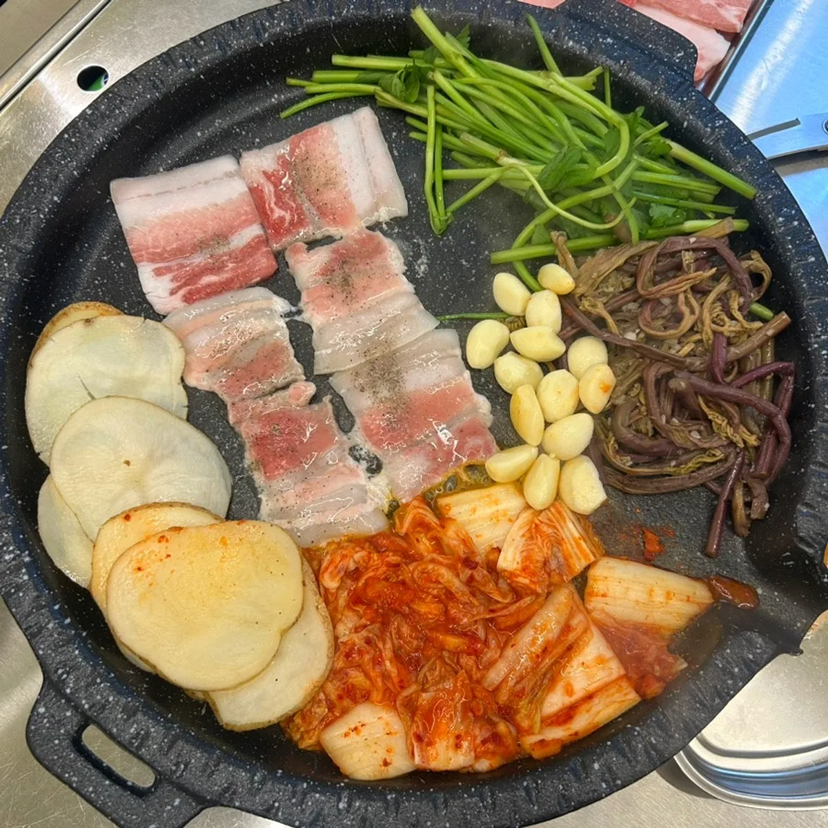 불판에서 익어가는 냉동삼겹살과 각종 구이 재료