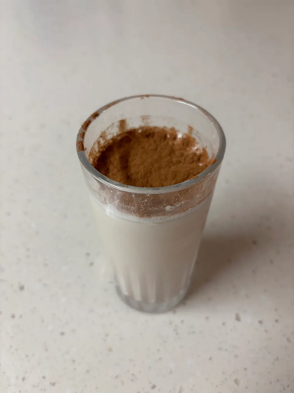 A glass of unsweetened oat drink next to the product package