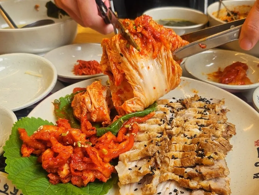 A bite of bossam topped with bossam kimchi and dried radish strips