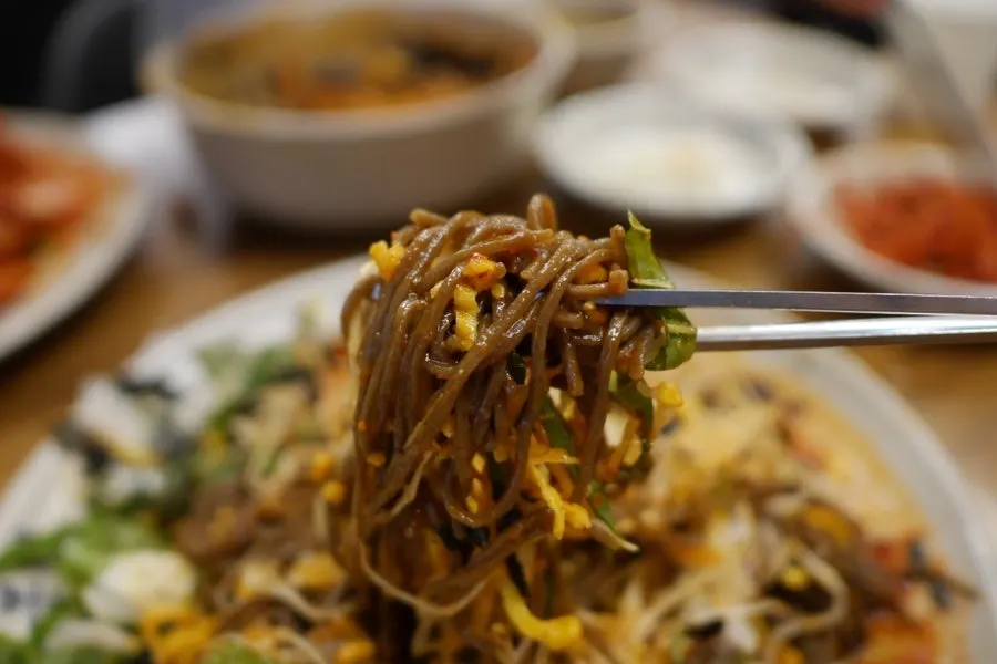 A bite of bossam topped with makguksu noodles