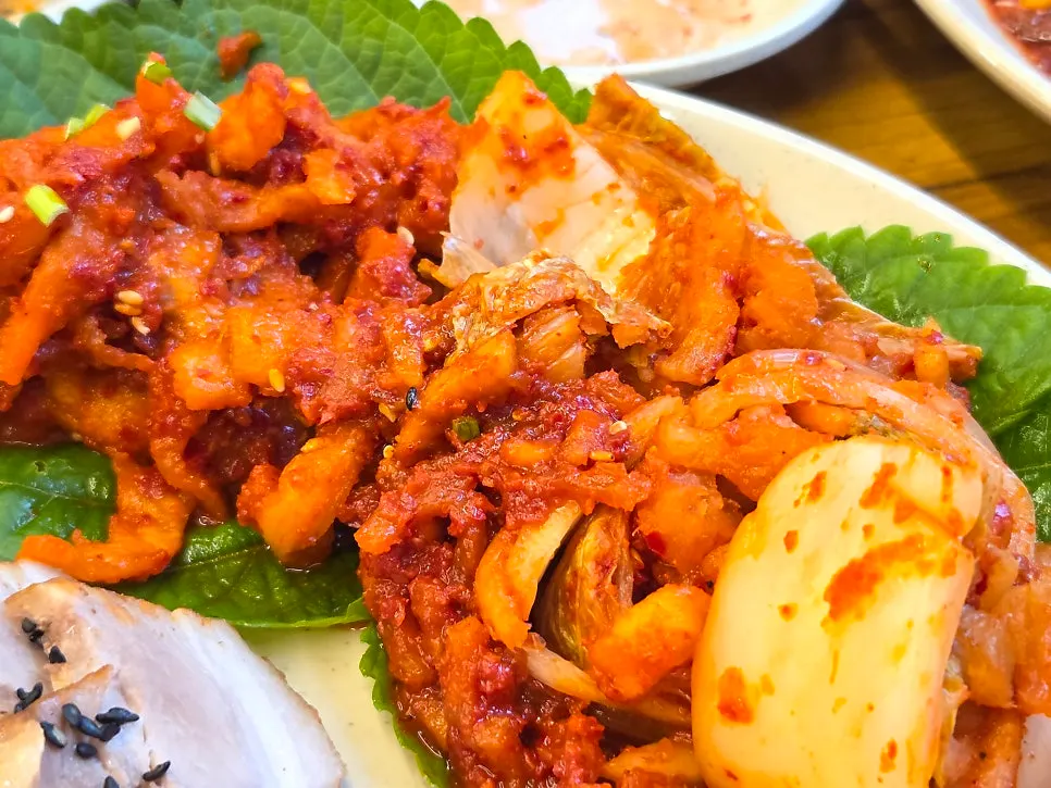 Red bossam kimchi next to a small plate of obong bossam