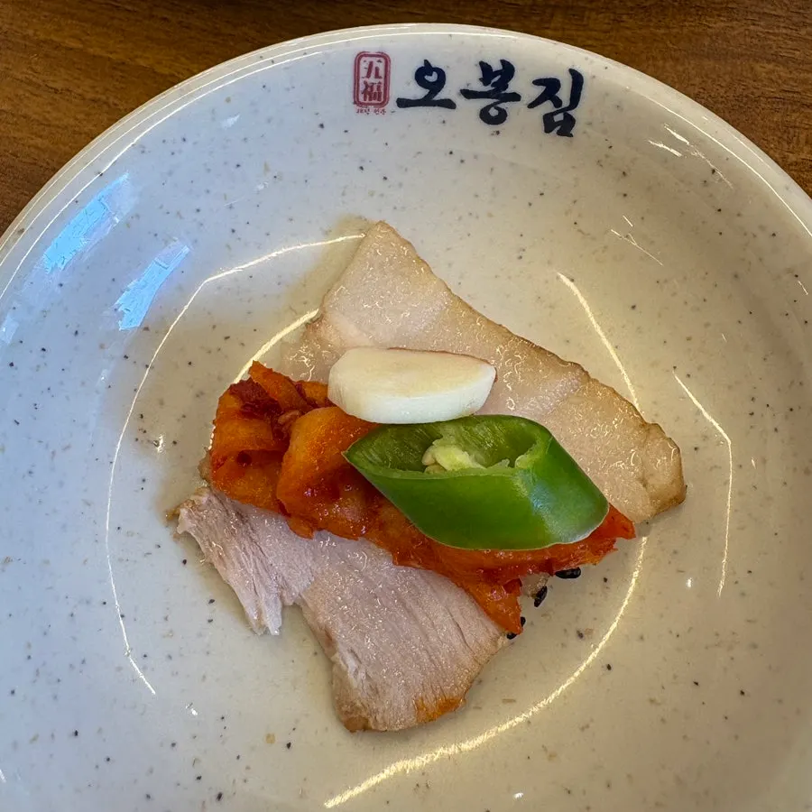 A bite of bossam topped with makguksu noodles