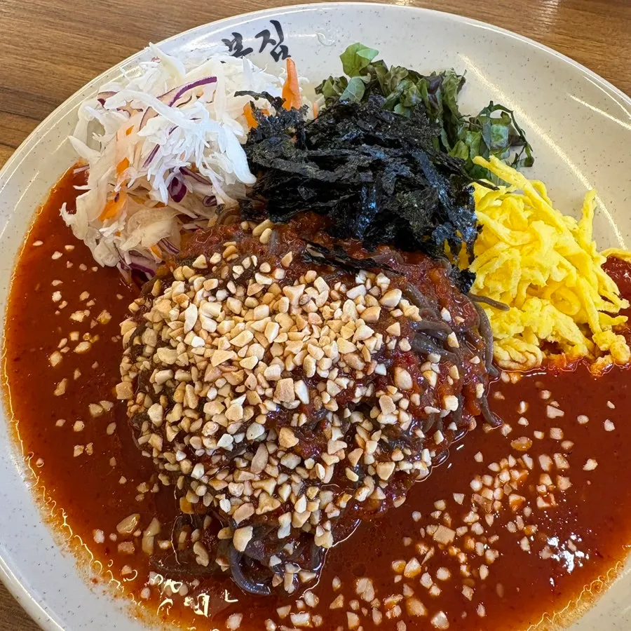 Makguksu noodles topped with egg garnish and nuts