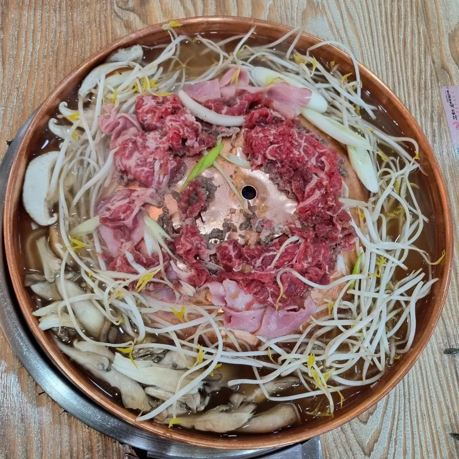 돌판 가장자리 육수에 버섯과 숙주를 익히는 모습