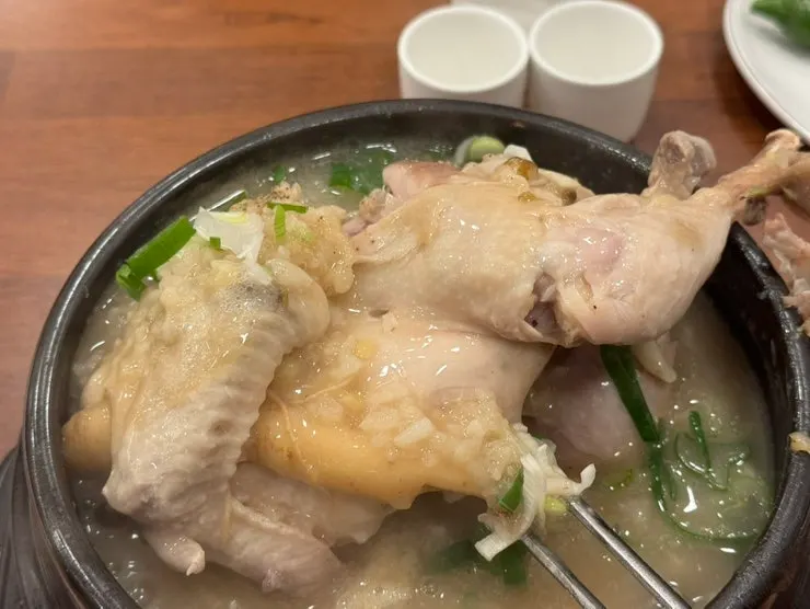 A whole chicken lifted out of the samgyetang broth