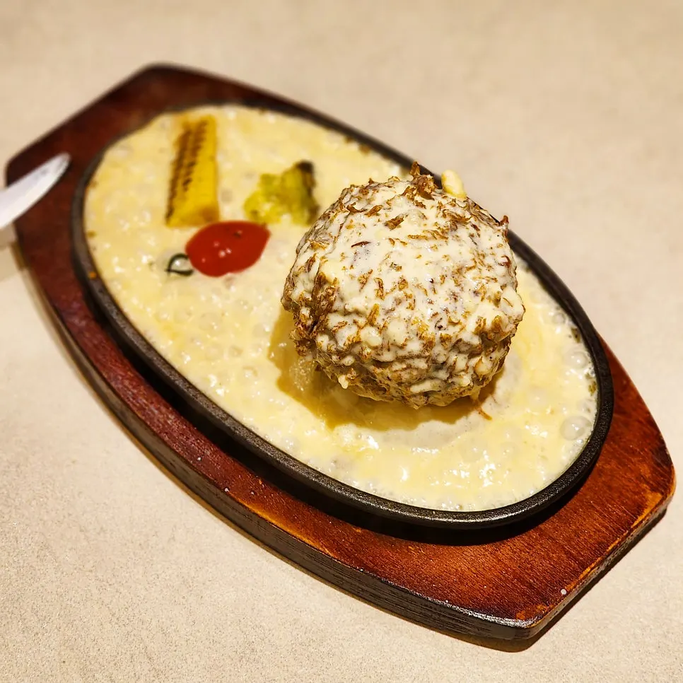 Cheese sauce being poured over sizzling cheese katsu on a hot plate