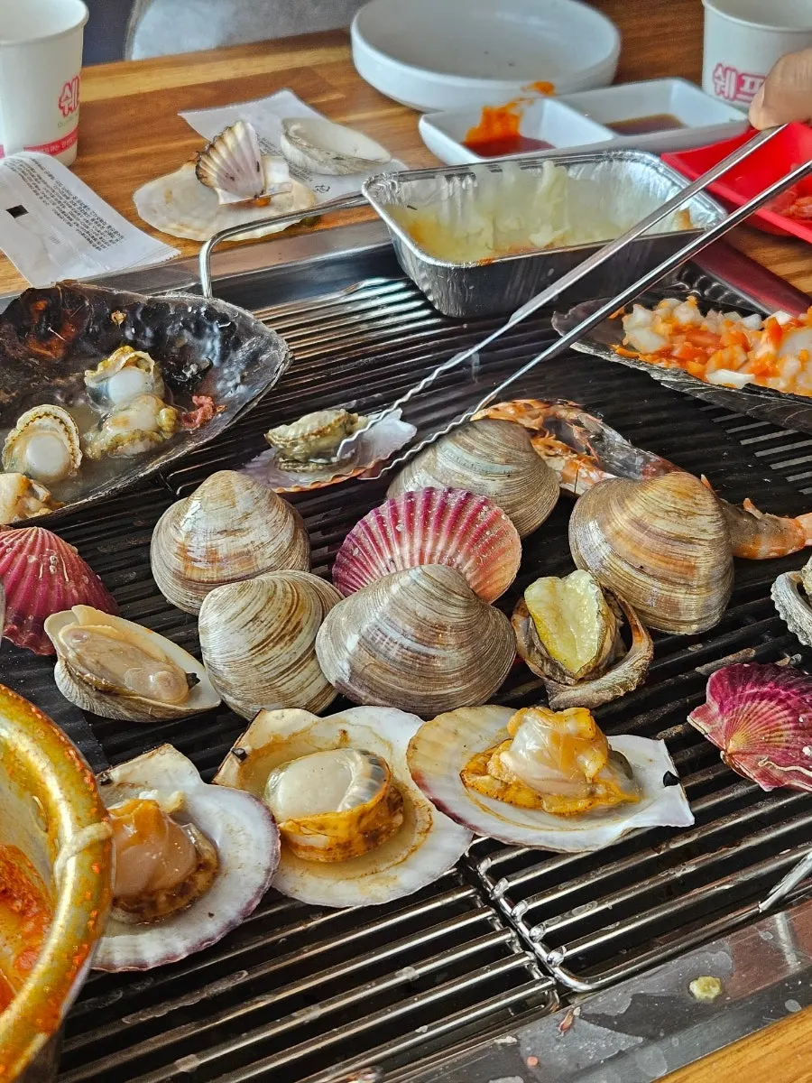 Full spread of grilled clams with cheese tteokbokki and vegetables