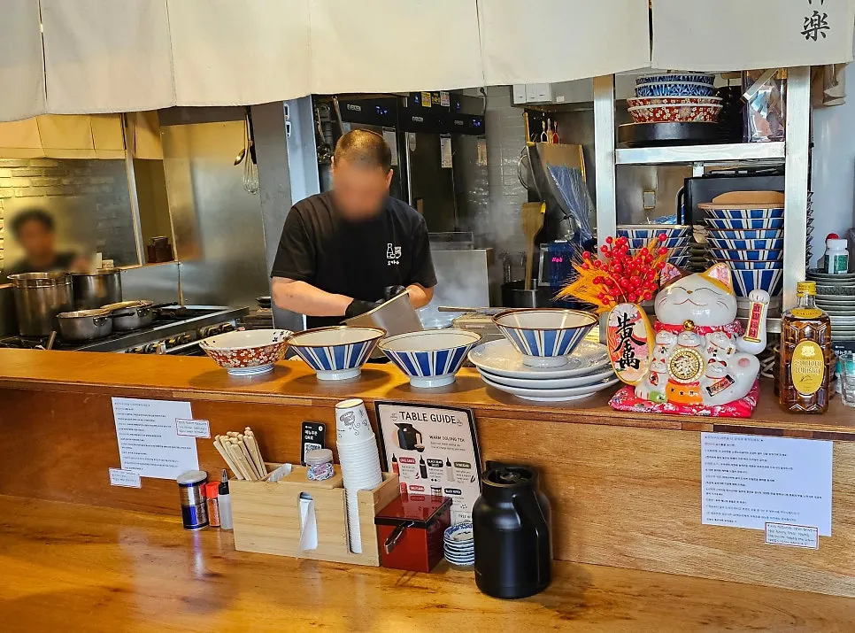 Warmly lit open-kitchen interior of Okagura Ramen