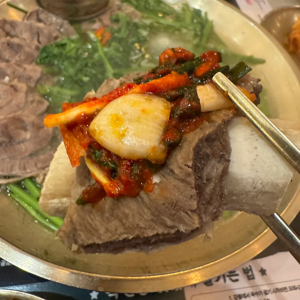 A bite of boiled pork topped with seasoned garlic and green onion kimchi