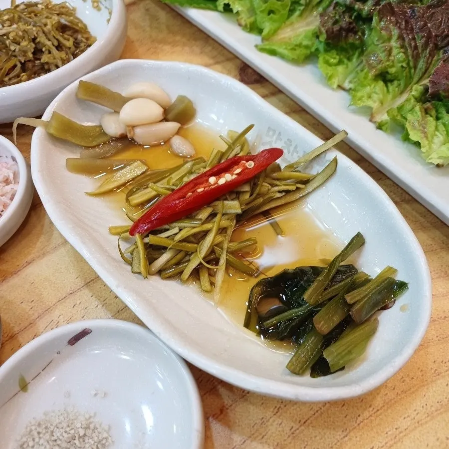 A spread of pickled side dishes including pickled chili and rinsed aged kimchi