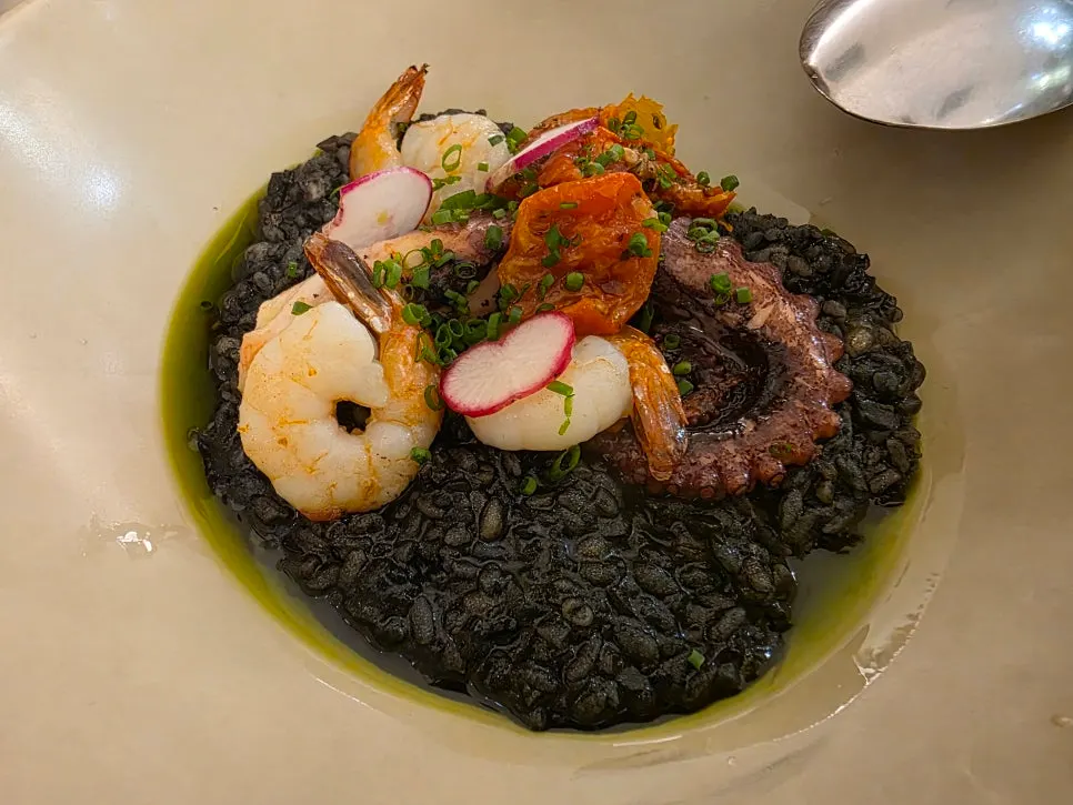 A plate of squid ink risotto topped with octopus legs and shrimp