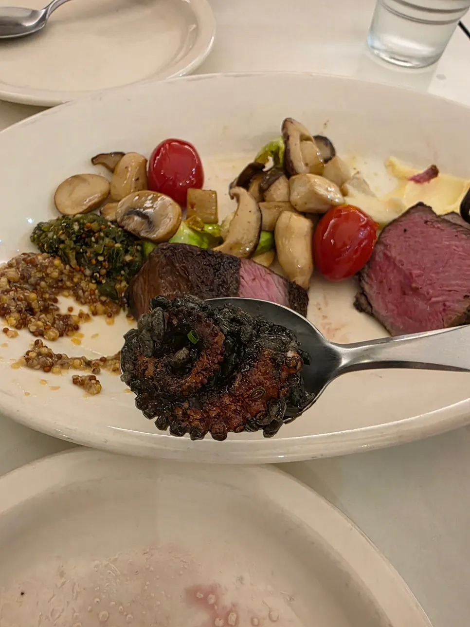 A spoon holding squid ink risotto and a piece of octopus leg