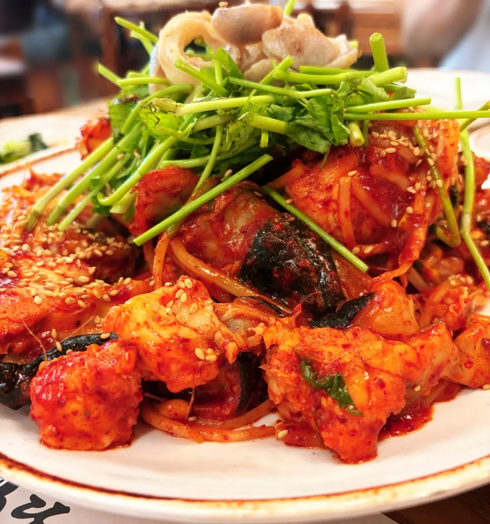 A plate of monkfish stew topped with bean sprouts and minari