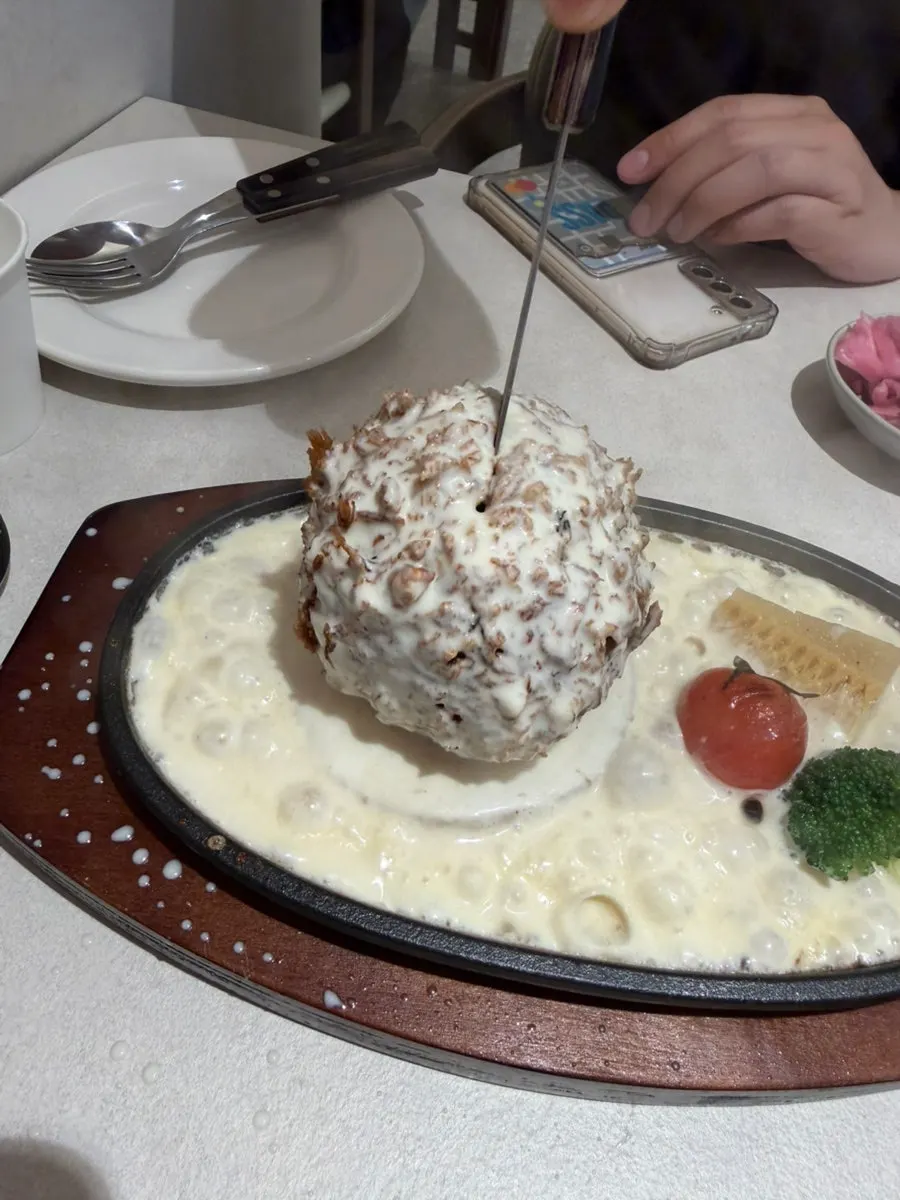Cream cheese sauce being poured over cheese katsu on a sizzling plate