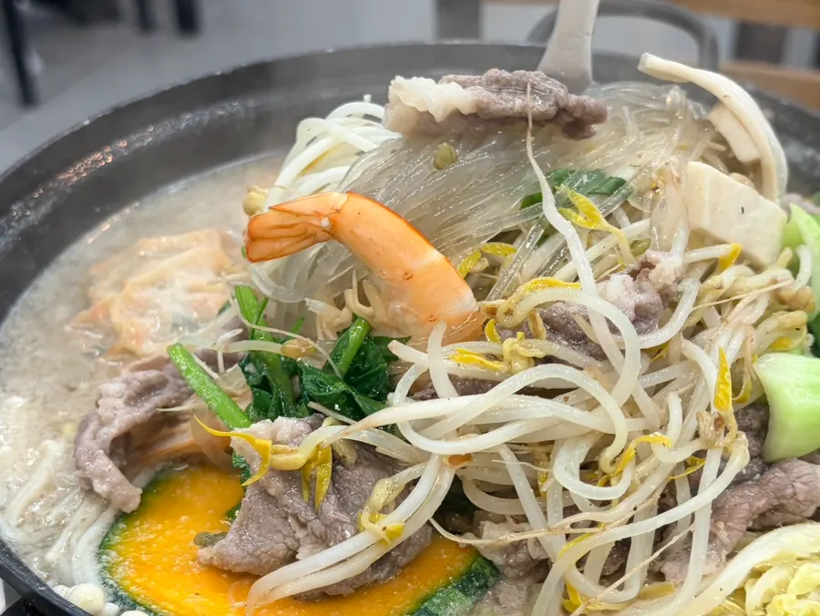A bowl of hot pot with vegetables and meat