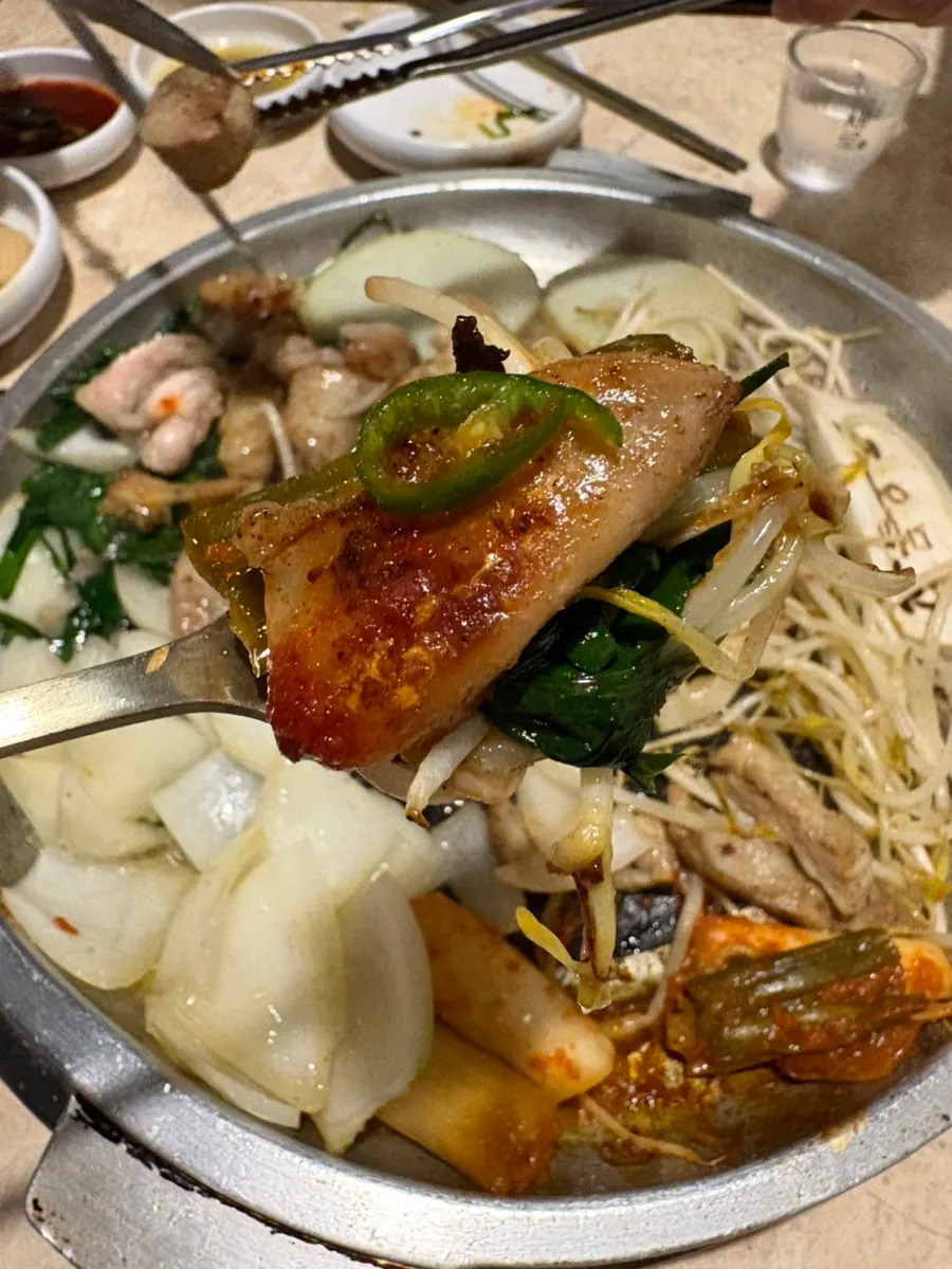 A piece of gopchang with bean sprouts, onion, and chives