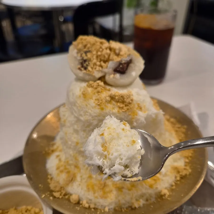 A spoonful of milk bingsu mixed with red bean and injeolmi powder