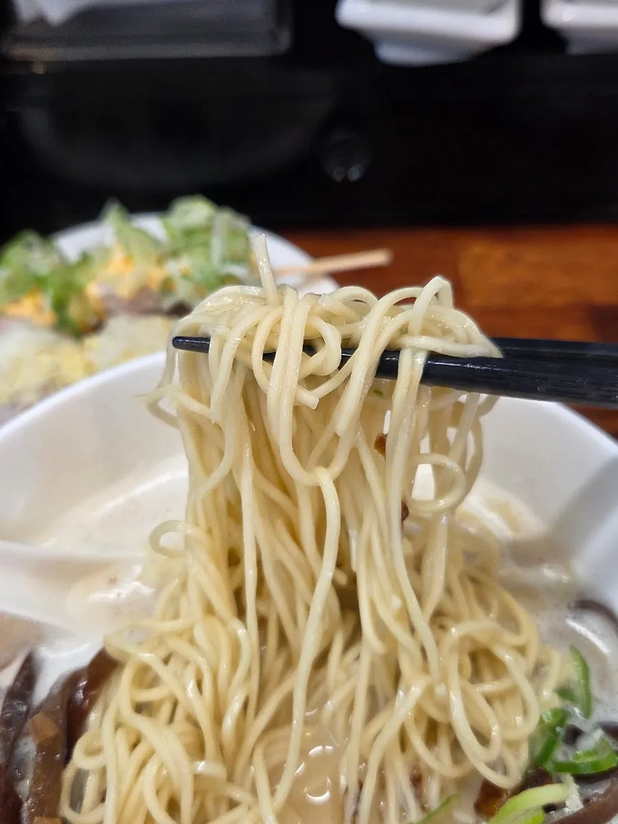 Thin ramen noodles lifted up coated in broth