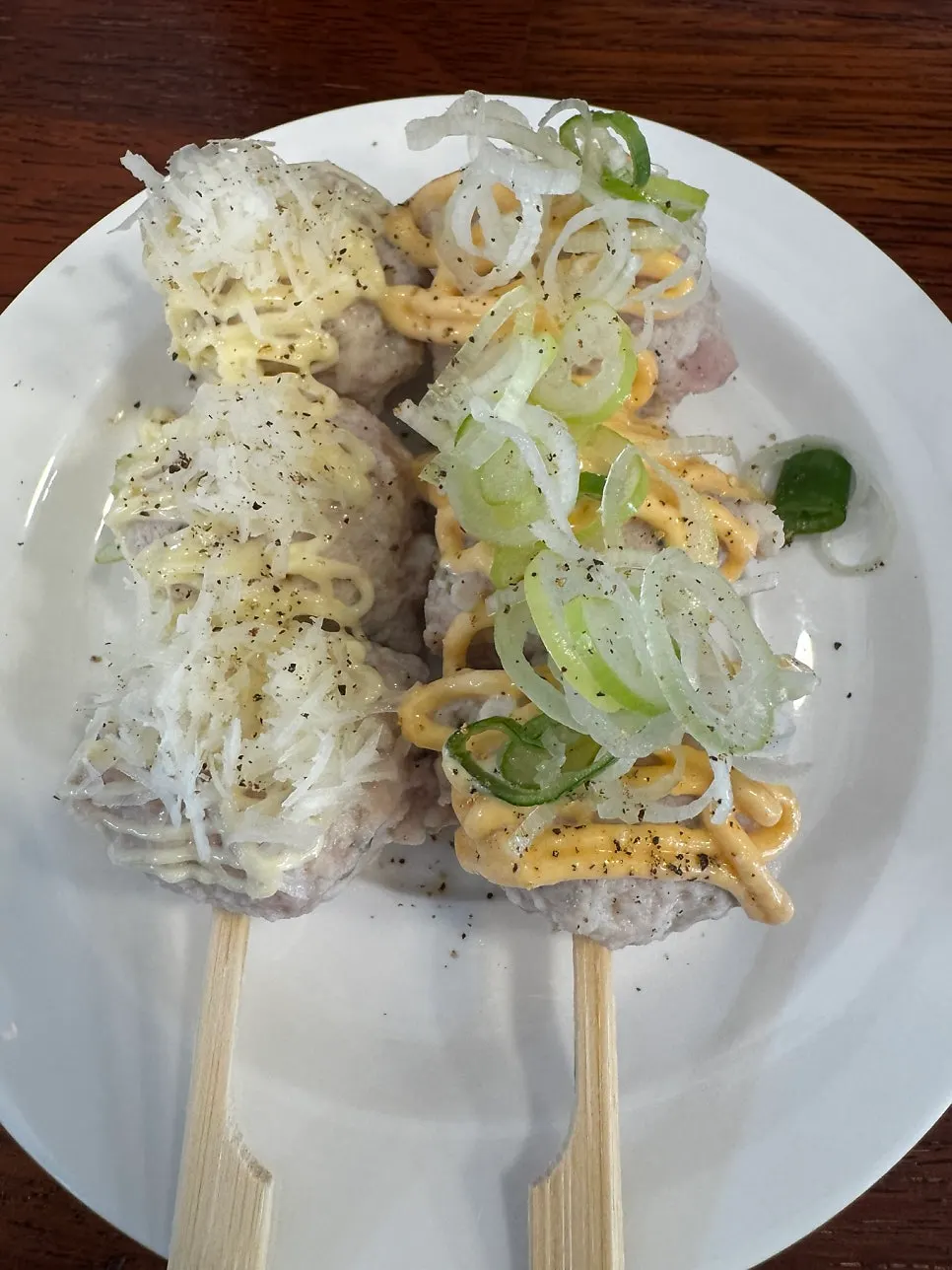 A plate of assorted tsukune with sauce and scallions