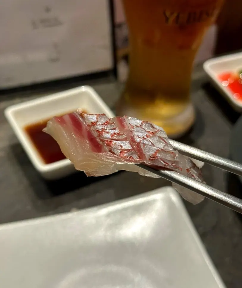 A piece of aged sea bream sashimi picked up with chopsticks