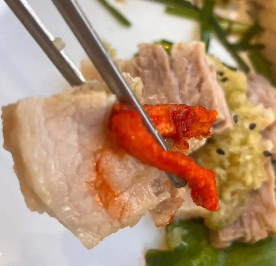 A piece of pork belly bossam topped with bossam kimchi and radish