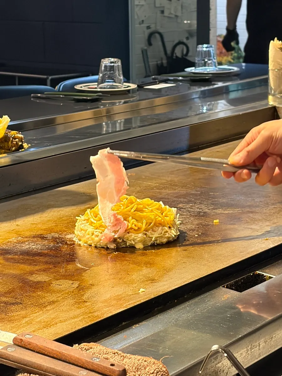 Modanyaki noodles and cabbage being stir-fried on the central teppan