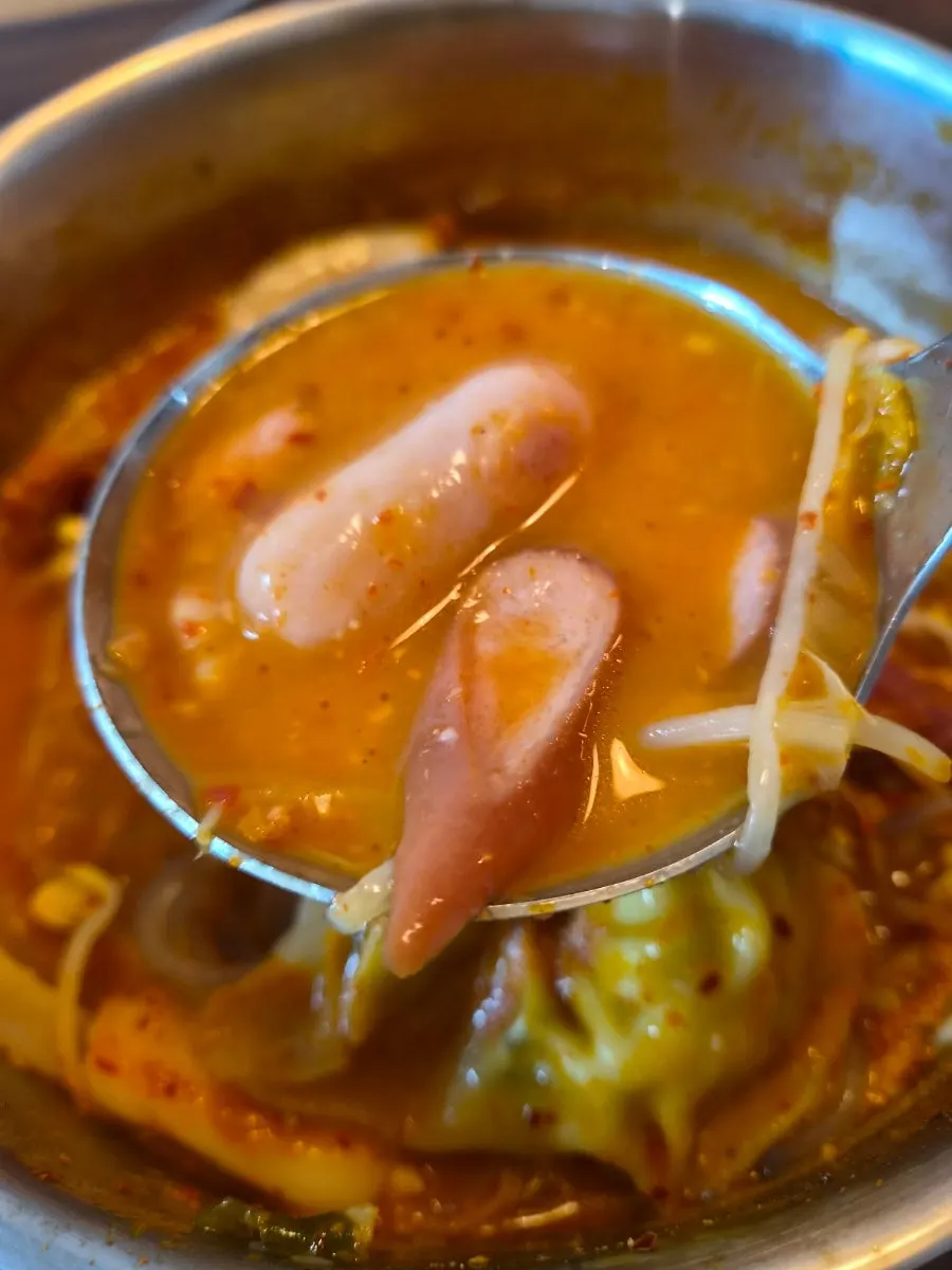 A ladle full of budae jjigae packed with ingredients