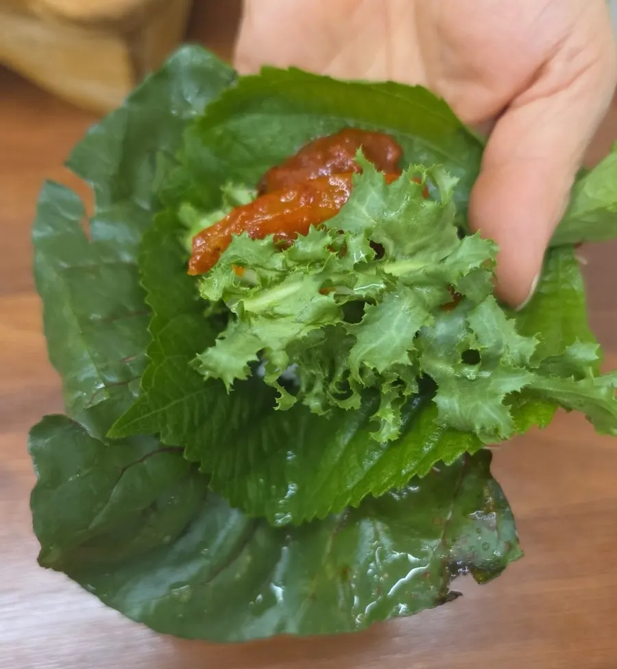 A wrap green topped with rice, pork, and gangdoenjang