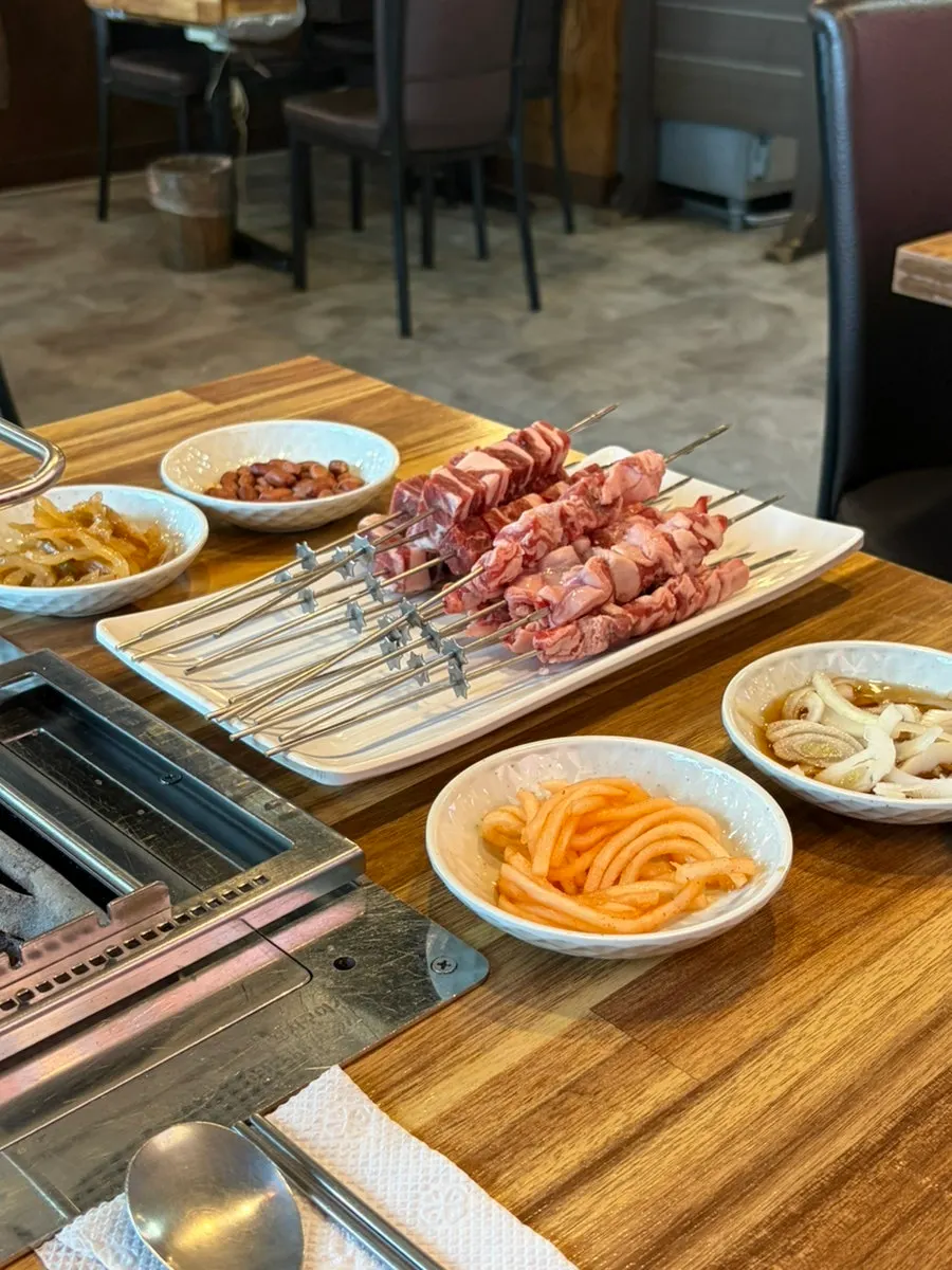 Table setup with banchan and seasoning alongside lamb skewers