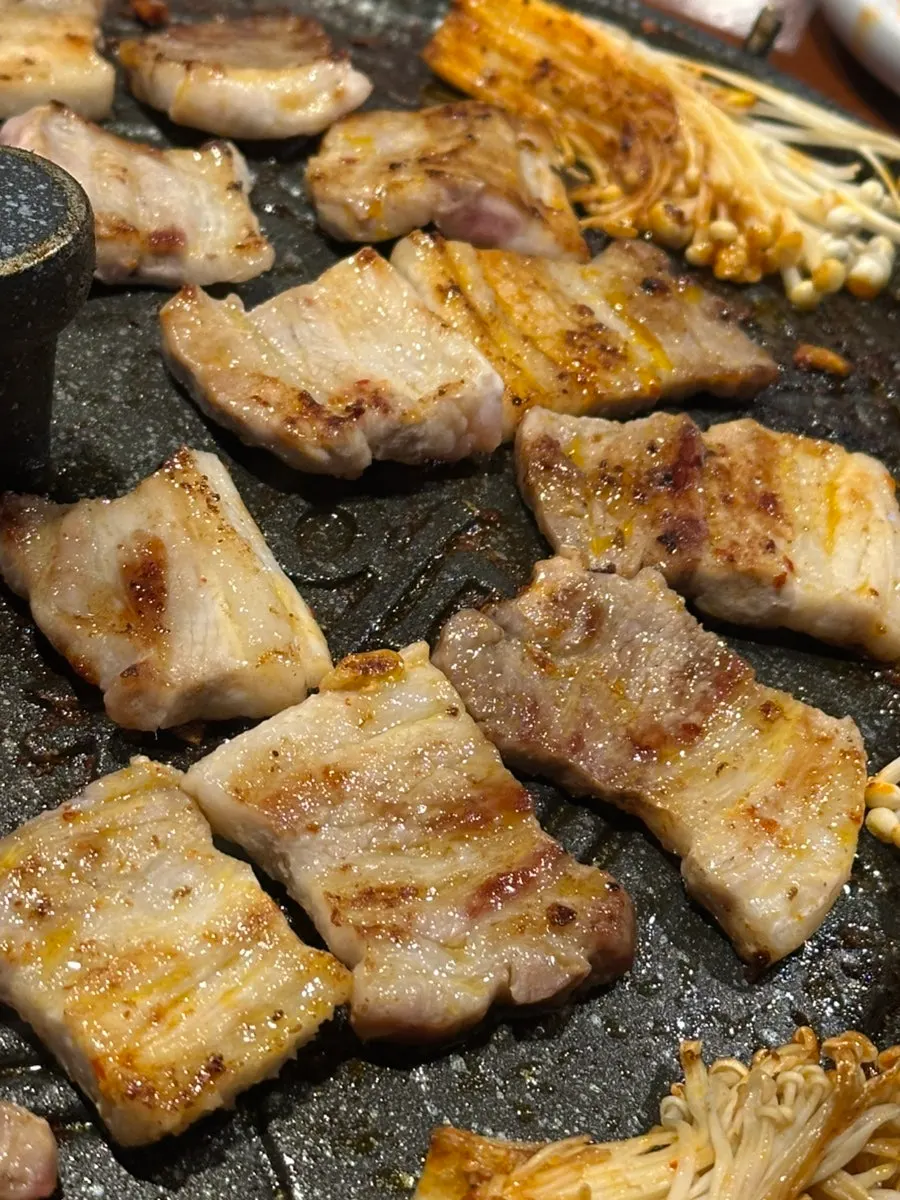 Meat, kimchi, and vegetables grilling on a pot lid