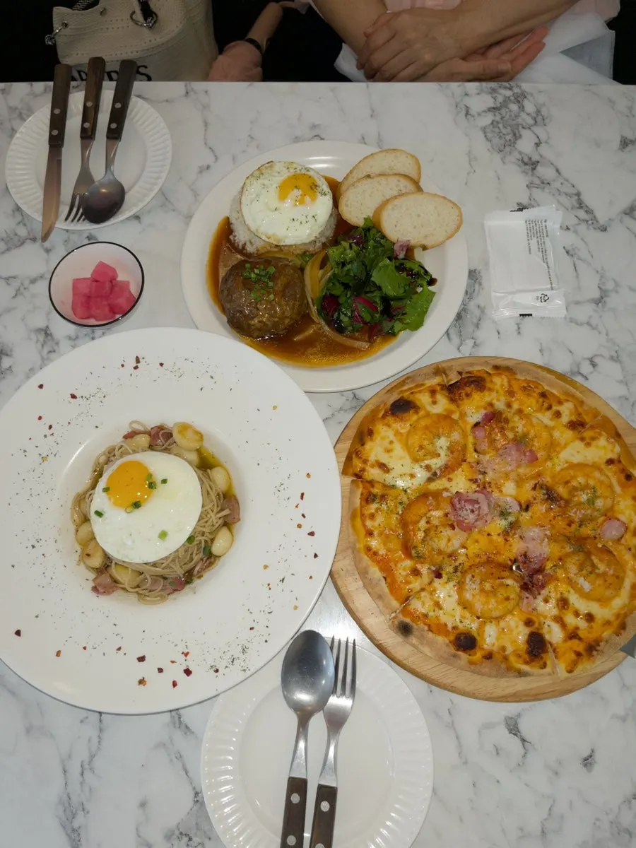 Table spread with pizza, pasta, and hamburg steak together