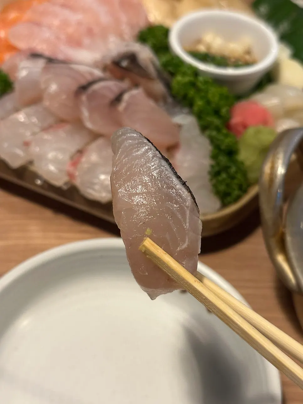 A piece of mackerel sashimi held with chopsticks