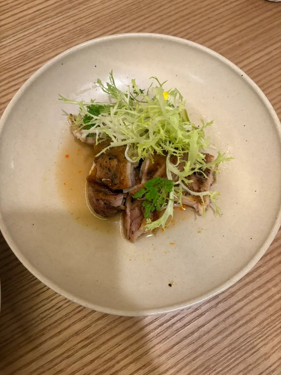 Grilled chicken thigh plated with frisée and herbs