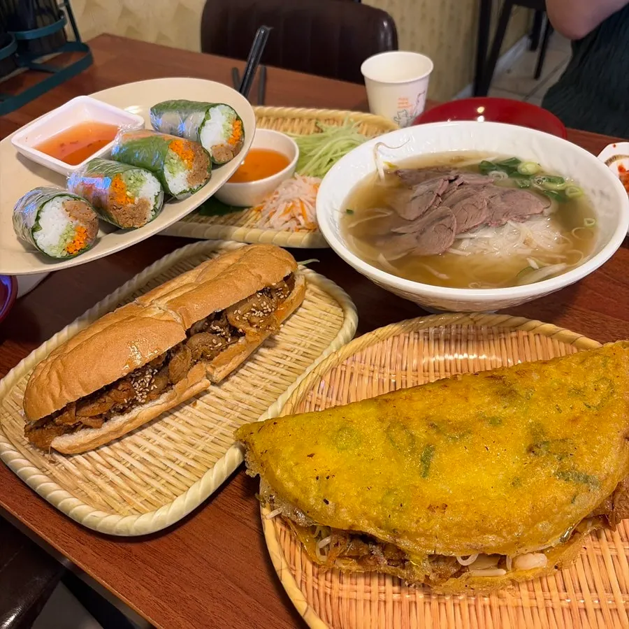 Pho, fresh spring rolls, bulgogi banh mi, and banh xeo laid out on the table