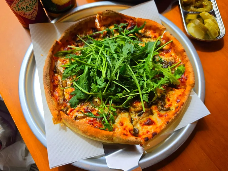 A slice of Surfer's pizza topped with cheese and arugula