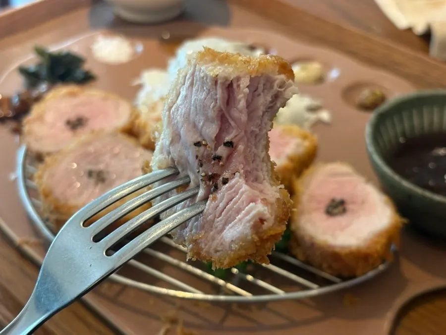 A bite-sized piece of tenderloin katsu picked up with chopsticks
