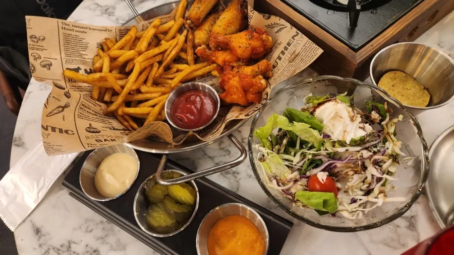 Table with salad, chicken wings, and beer