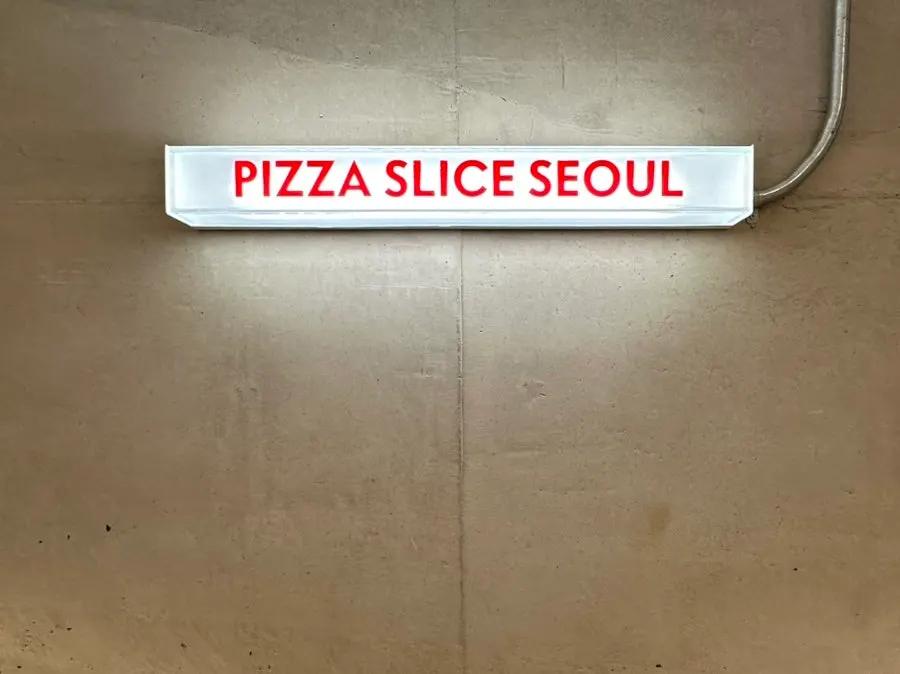 Red PIZZA SLICE SEOUL sign hanging on the wall